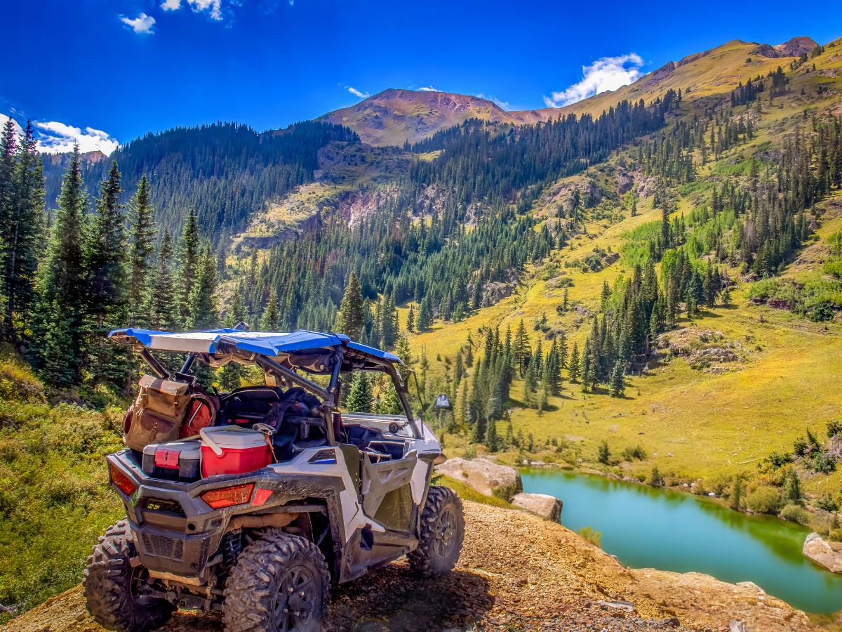 An SXS rental on a rugged off-road trail with a scenic lake in the background